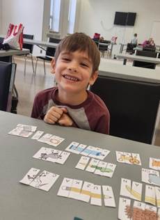 A child sitting at a table with cards on it

Description automatically generated